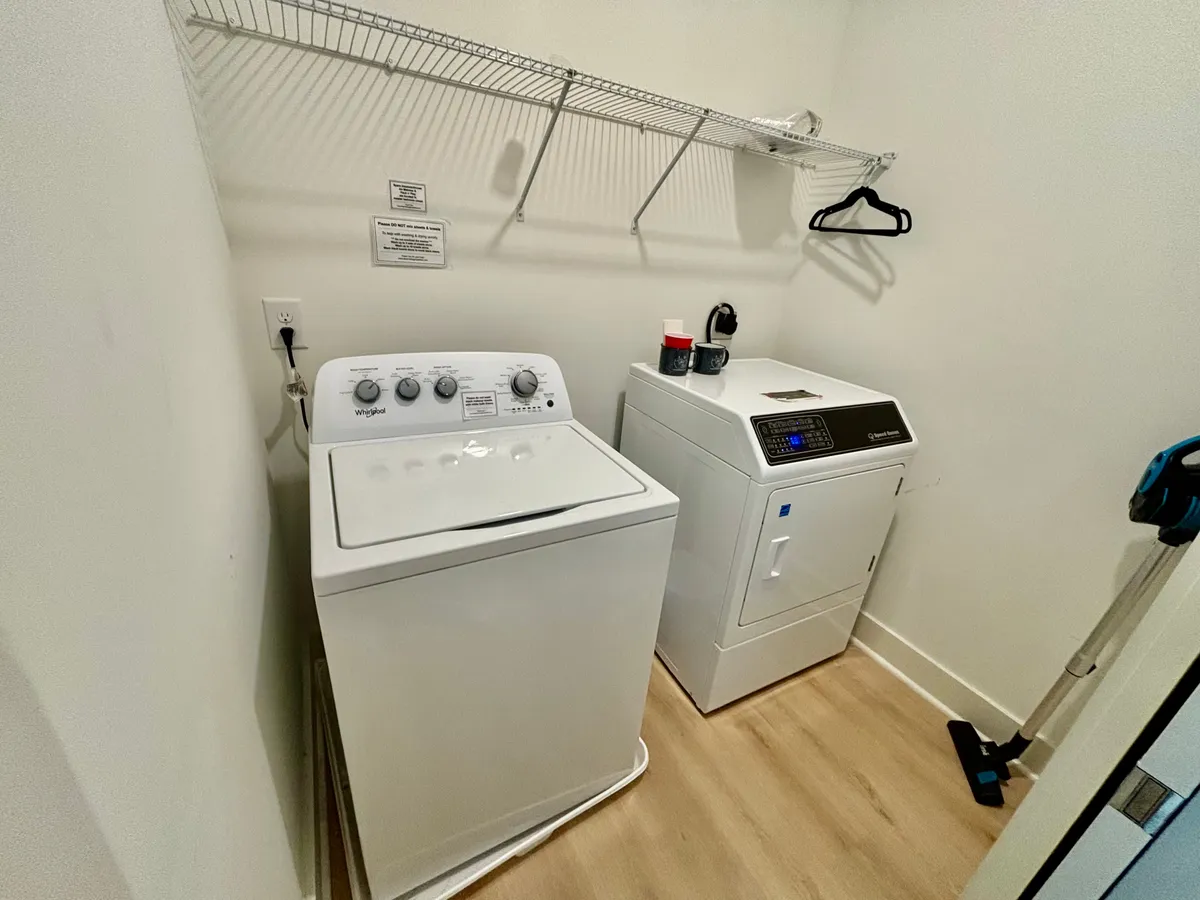 A practical laundry area with a washer, dryer, and overhead shelf for organization. The scene underscores convenience, tidiness, and the ability to handle laundry needs effortlessly during a stay.