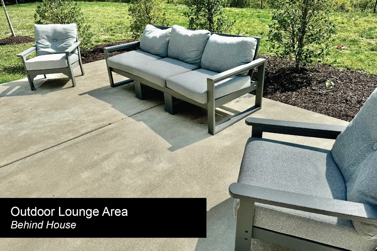 A comfortable outdoor lounge area with a sofa, lounge chairs, green grass, and well-kept bushes, providing a tranquil spot for unwinding after work or for informal team gatherings in a relaxed setting.