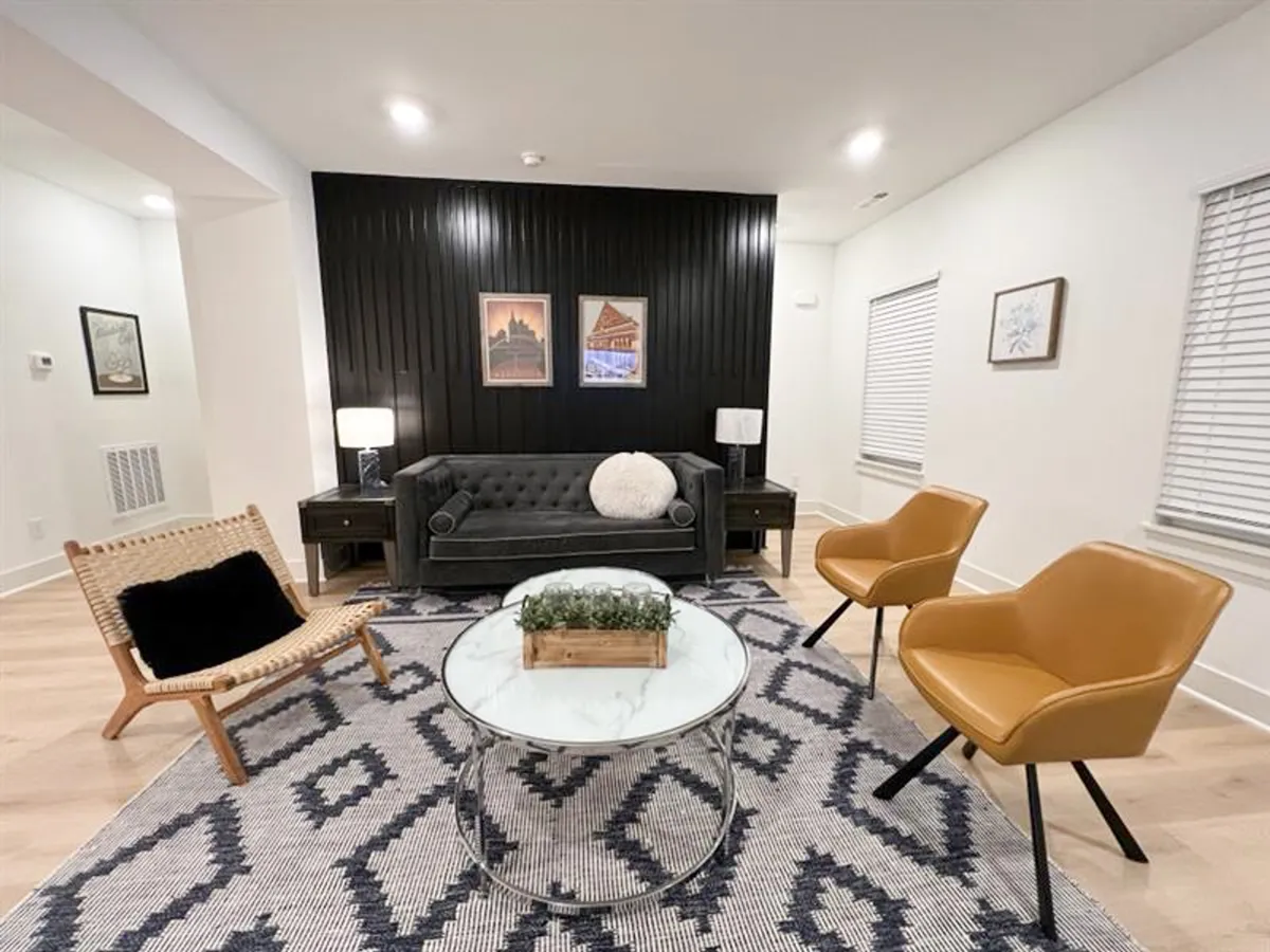 The image shows a modern, cozy living space with a black accent wall adorned with artwork, a contemporary sofa, and a round coffee table. The atmosphere is inviting, stylish, and comfortable—ideal for relaxing or socializing after a day out.