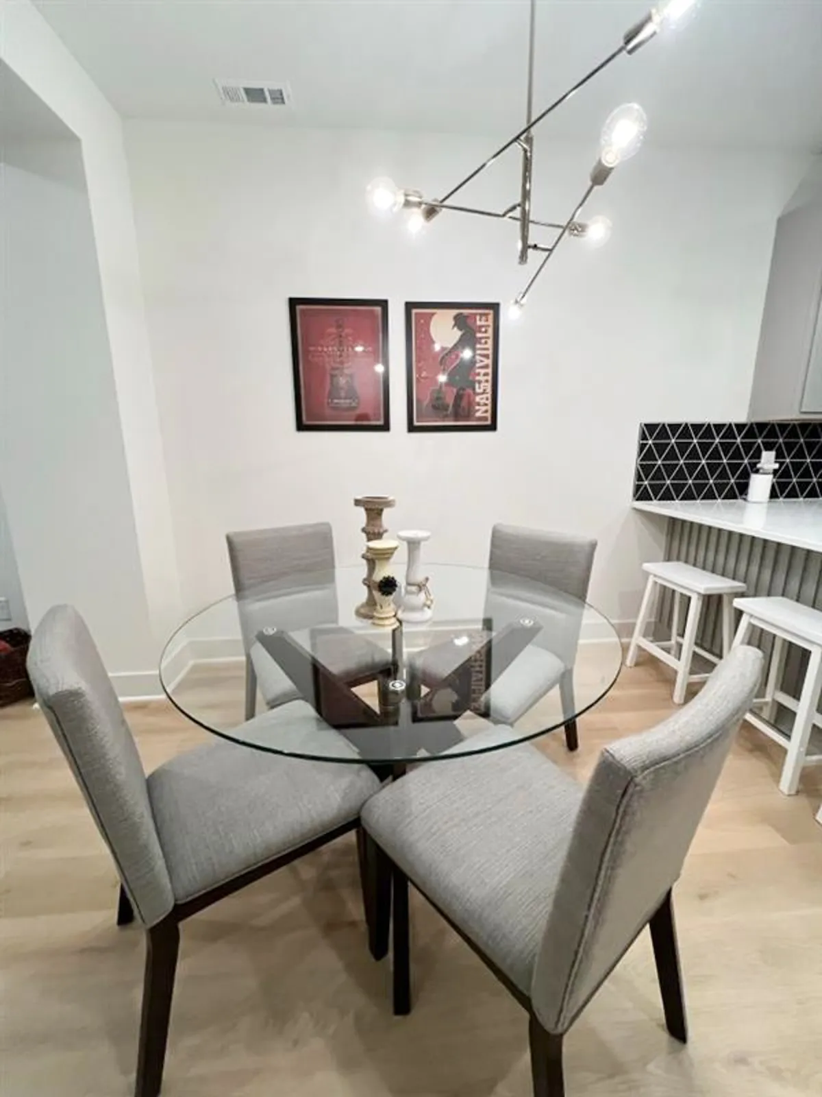 A stylish dining area featuring a glass table, modern chairs, a unique light fixture, and contemporary artwork. The setting is intimate yet functional, inviting conversation and togetherness during meals.