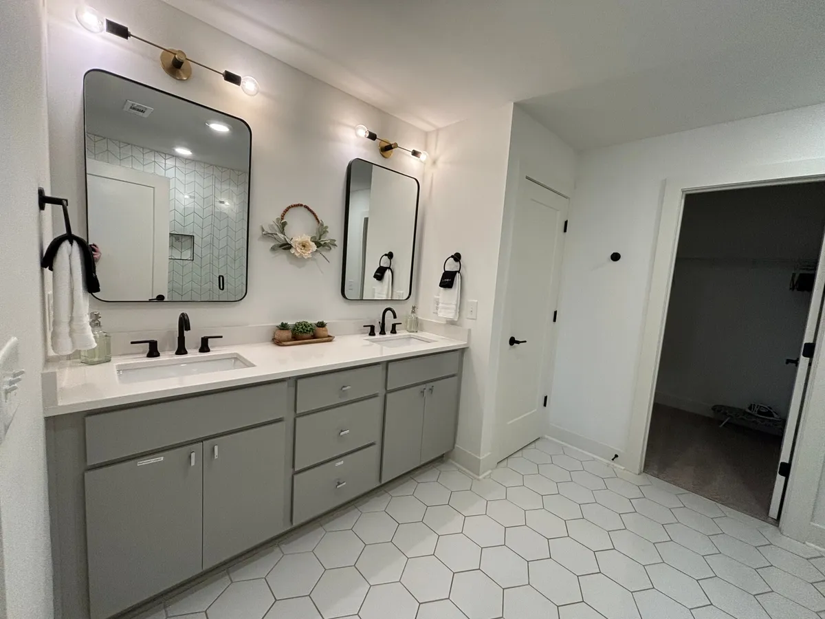 A modern bathroom featuring a double sink vanity with large mirrors, decorative wreath, and stylish hexagonal tile flooring. The space is bright, spacious, and designed for convenience during morning and evening routines.