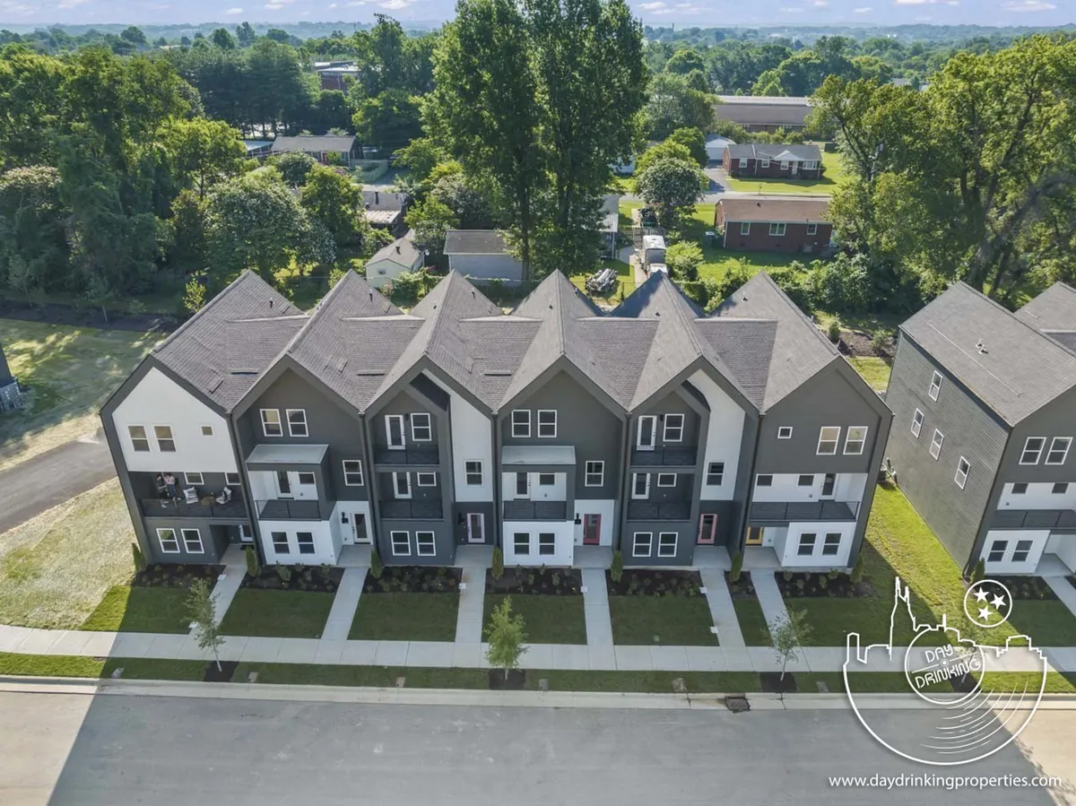 A row of modern townhouses lines a well-manicured street, set beneath a clear blue sky. The landscaping is neat and inviting, evoking a sense of community and relaxation where families can gather for outdoor fun.