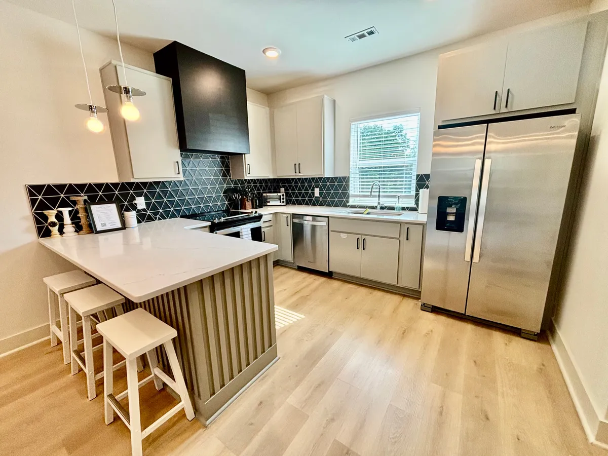 A bright, contemporary kitchen featuring an island with seating, a striking black and white backsplash, and stainless steel appliances. The open design is inviting, making it easy for the chef to interact with guests or family during meal preparation.