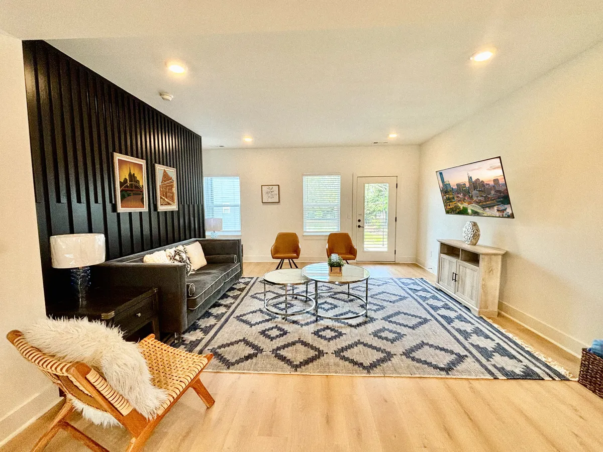 The hero image showcases a stylish, welcoming living area with a striking black accent wall, plush sofa, modern coffee table, vibrant artwork, and streams of natural light from large windows, creating an inviting space for guests to relax, socialize, or unwind after exploring the city.
